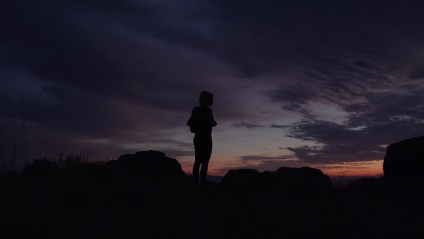 A woman stands silhouetted against a colorful sunset sky
