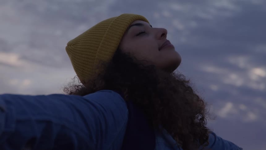 Woman with curly hair and a yellow cap opening her arms outdoors
