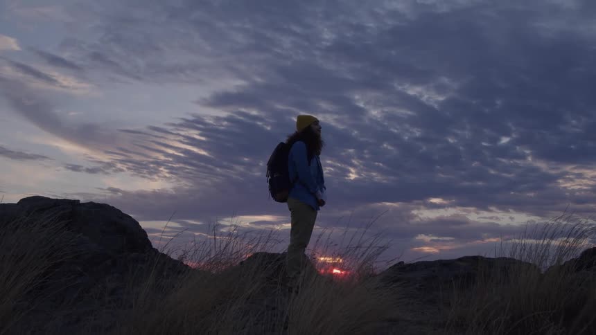 Hiker standing on rocks as the sun sets on the horizon