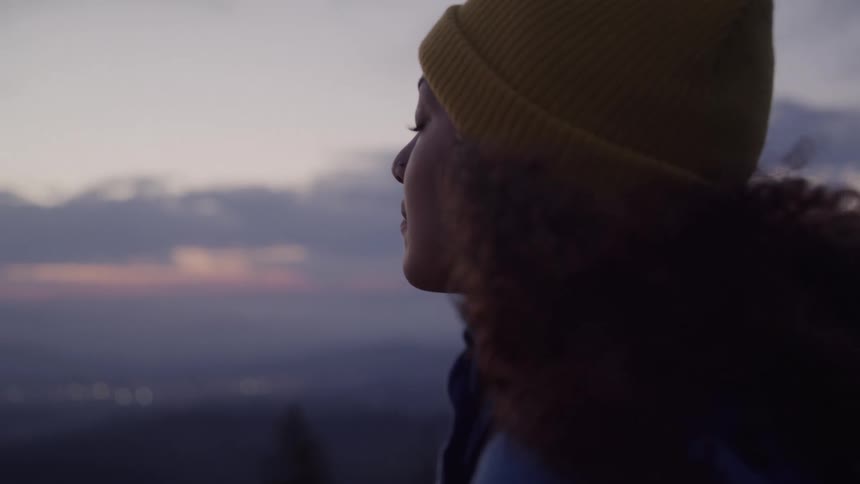 A smiling woman with her eyes closed enjoying fresh air on her face as the sun sets