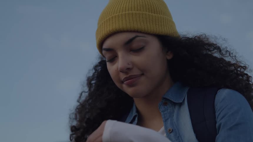 Woman wearing a yellow beanie and backpack looking down