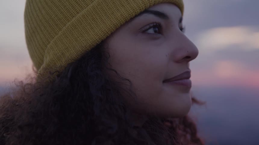 Woman wearing a yellow beanie looking up and smiling