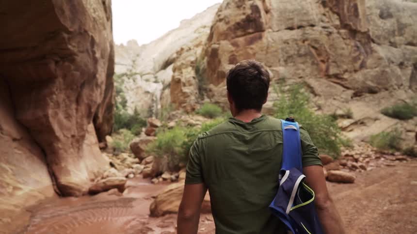 Man hiking through desert mountains and canyons with a backpack over his shoulder
