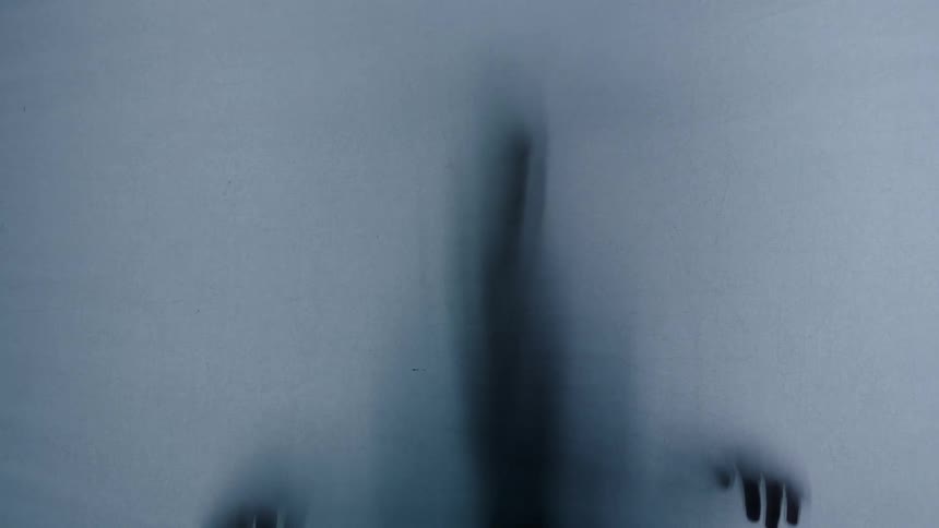 Blurred shadow of a person with palms pressed against a translucent surface