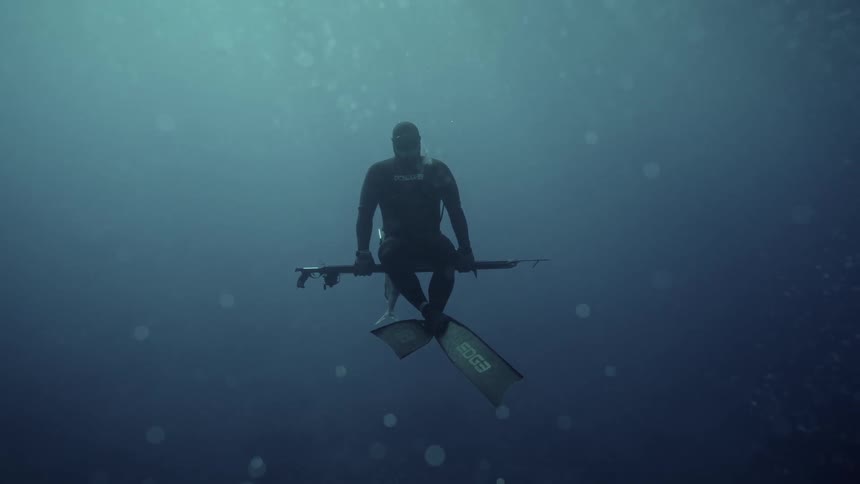 A person wearing flippers diving into the bottom of the water and holding a spear gun