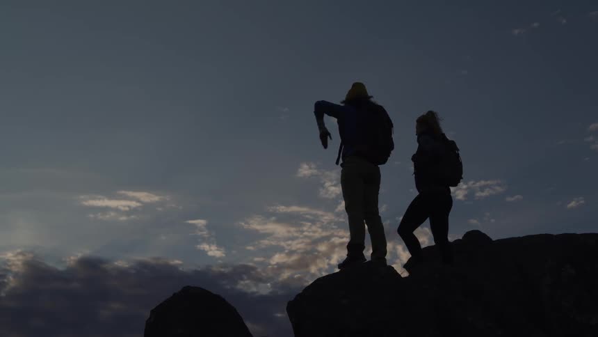 Two hikers on a rock clapping their hands in the late afternoon