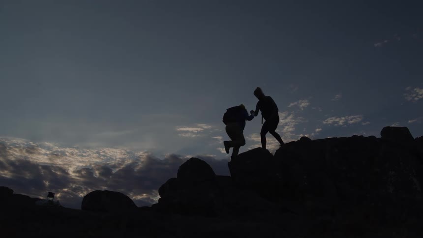 A person helps a friend climb up the mountain