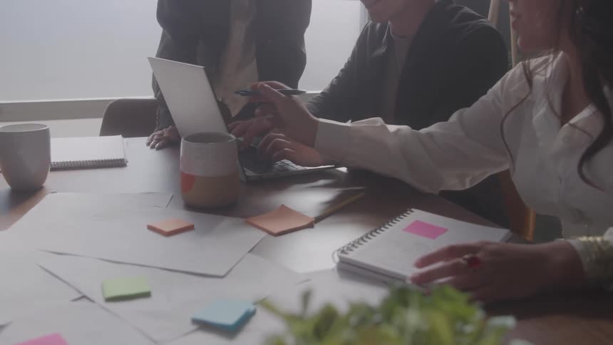 Three coworkers talk and look at a laptop together