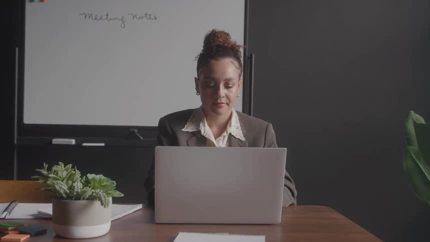 Woman working on a laptop with a notes board in the background