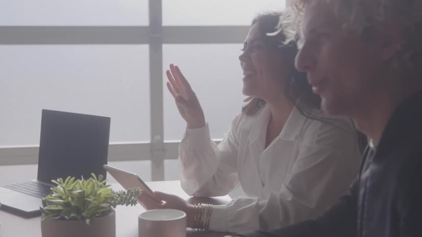 Man and woman sitting at an office desk talking smiling