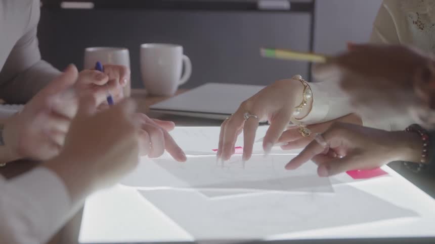 Group of people gesturing and pointing at documents on a lit table