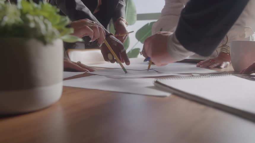 Hands of several people working together on notes and documents over a meeting table