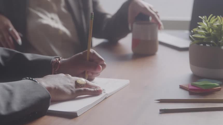 Hands writing in a notebook during a work meeting