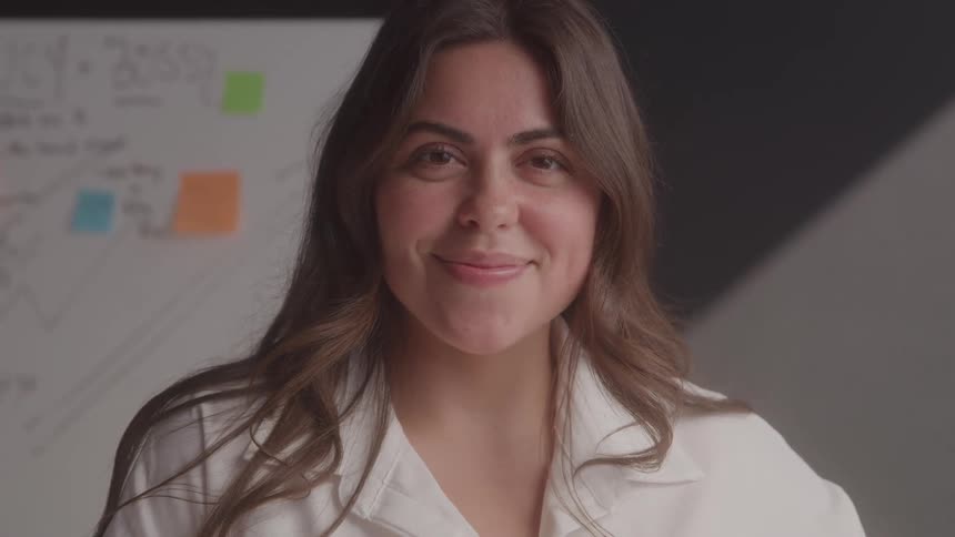 A young woman stands in front of a class facing away from the whiteboard with a series of texts written on it smiling at midday