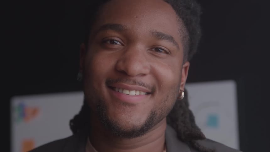 Smiling man with long hair tied back wearing an earring and blazer