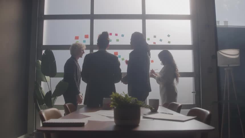 Four people standing in front of a glass wall with colorful sticky notes