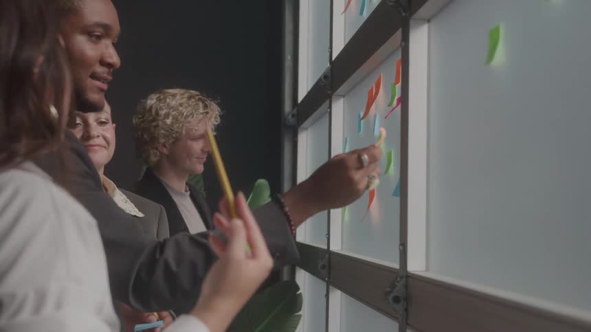 A group of four students stands in front of a window picking sticky notes off the glass at midday