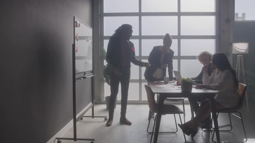 Four people working together with one writing on a whiteboard and the others gathered at a table
