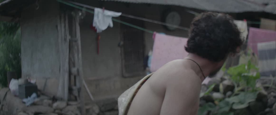 A woman holding a baby walks past a shirtless man