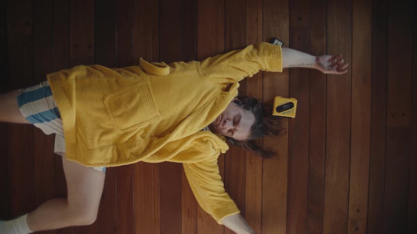 Person lying on a wooden floor wearing a yellow robe and headphones