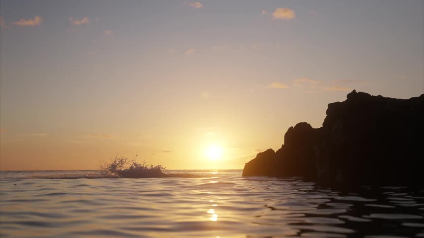 Person jumping from a rock into the sea at sunset