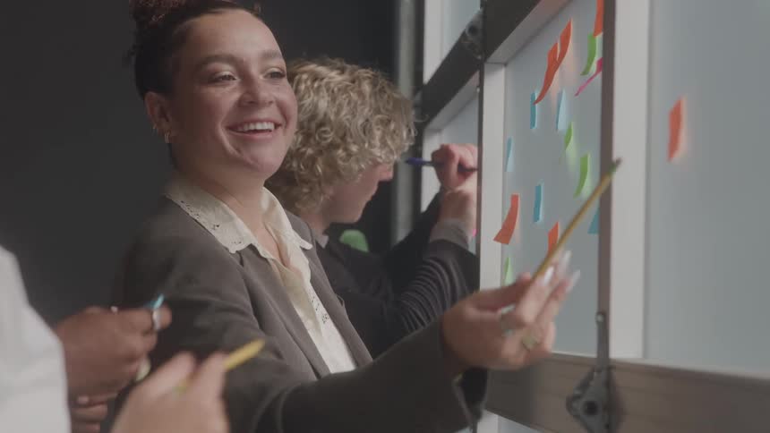 Woman smiling while placing colorful sticky notes on a glass surface