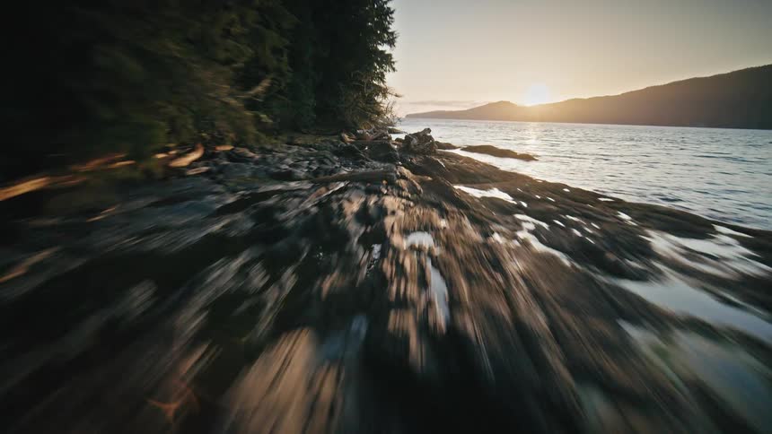 Rocks and trees along a coastal cliff as the sun sets on the horizon