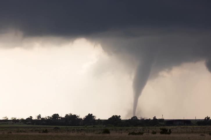 A powerful tornado spins across flat grasslands under dark storm clouds