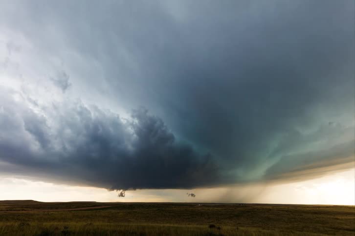 The video shows an ominous dark cloud formation or storm cloud hovering over a field of dry grass the camera pans from left to right revealing the vast expanse of the field under the dramatic sky
