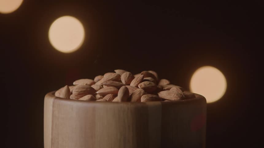 Wooden bowl filled with almonds with blurred lights in the background