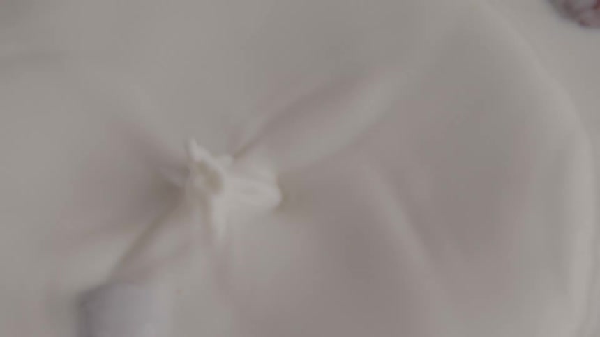 The video shows an egg being cracked into a bowl of milk or cream with the yolk and white separating as they fall into the liquid the egg is cracked offscreen and only the contents are shown dropping into the bowl
