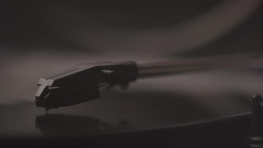 A close view of a record player shows the black stylus which is sitting on a spinning vinyl record