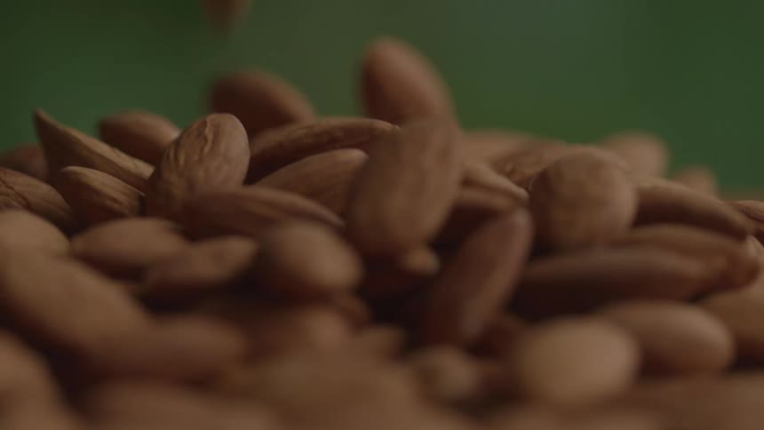 Falling almonds form a pile against a green background