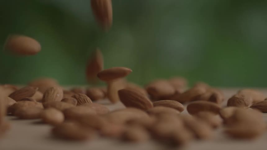 Falling almonds cover a flat pale rose surface against a green background