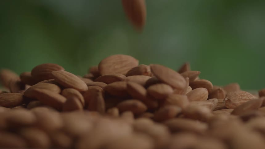 A stream of whole almonds falls onto a growing pile