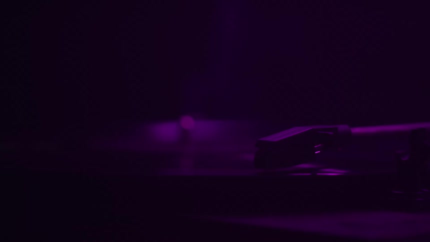 Turntable tonearm on a vinyl record lit by soft purple light
