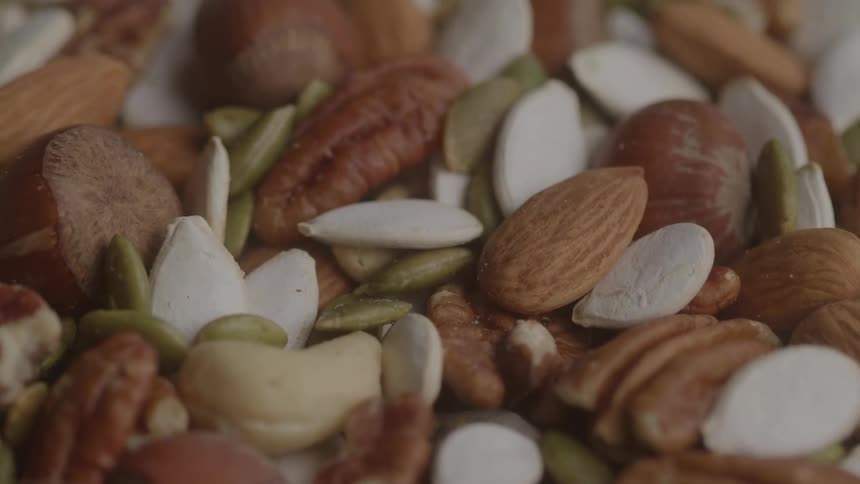 A mix of assorted nuts and seeds including almonds pecans cashews pumpkin seeds and sunflower seeds fills the frame
