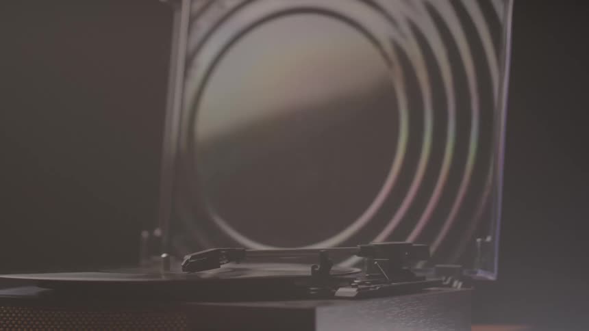 A record player sits beneath a partially open dust cover with circular reflections visible on the lid
