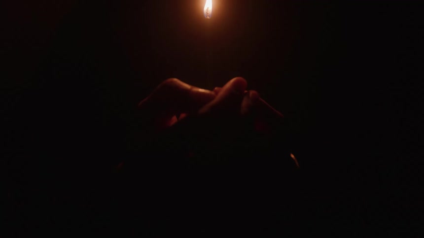 A persons arm holds a lit candle inside a dark room at night