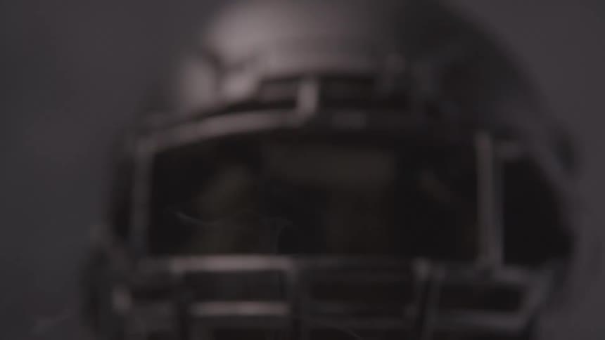 A dark football helmet is shown closeup under dramatic lighting