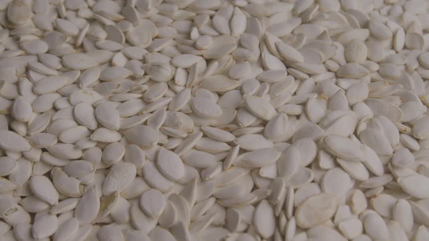 A large quantity of white pumpkin seeds is scattered evenly across the surface