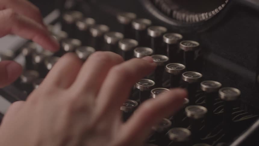 The video shows a closeup of a persons hands typing on a vintage typewriter the persons fingers press down on the keys and the carriage shifts as they type