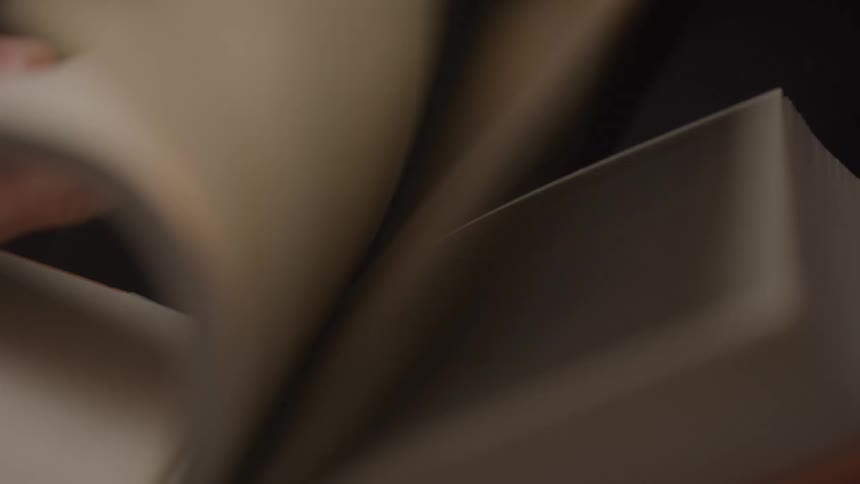 A hand quickly flips through the pages of a book creating a blur of paper the books pages are blank or unprinted suggesting it may be a notebook or journal