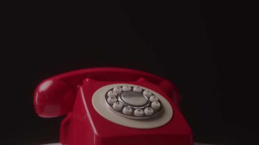 A vintage red rotary telephone sits against a black background