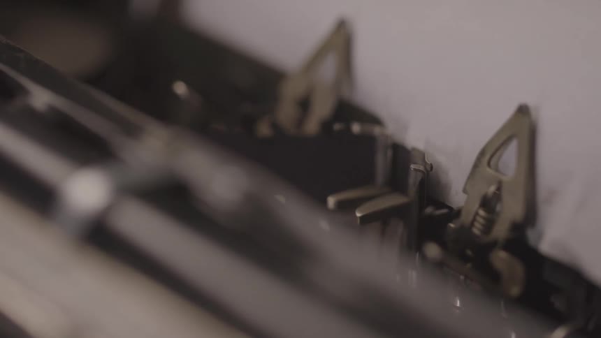 A typewriters hammers strike the paper printing letters as they move the shot focuses on the intricate mechanics of the vintage machine as it works