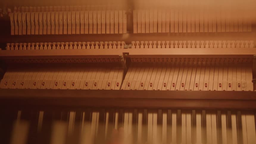 A close view from above shows the inside of a piano with its hammers and strings as a persons hand presses the keys causing the corresponding hammers to hit the strings