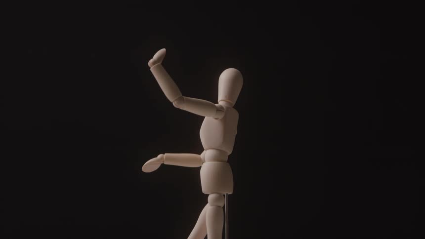 Wooden artist manikin holds a pose against a dark background