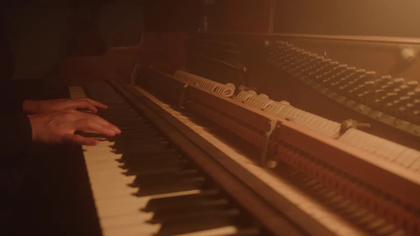 A close view of a piano shows a persons hands playing the keys with the lid open to reveal the hammers and strings moving inside