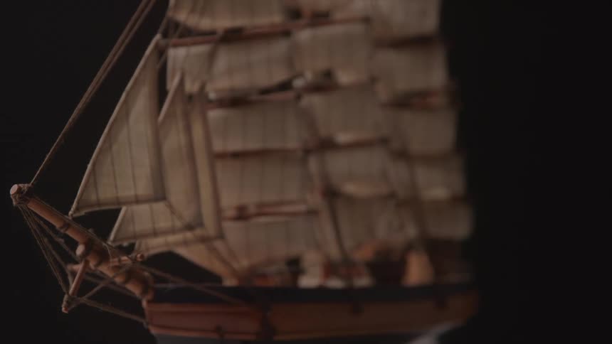 A detailed model ship with multiple sails and rigging is shown against a dark background