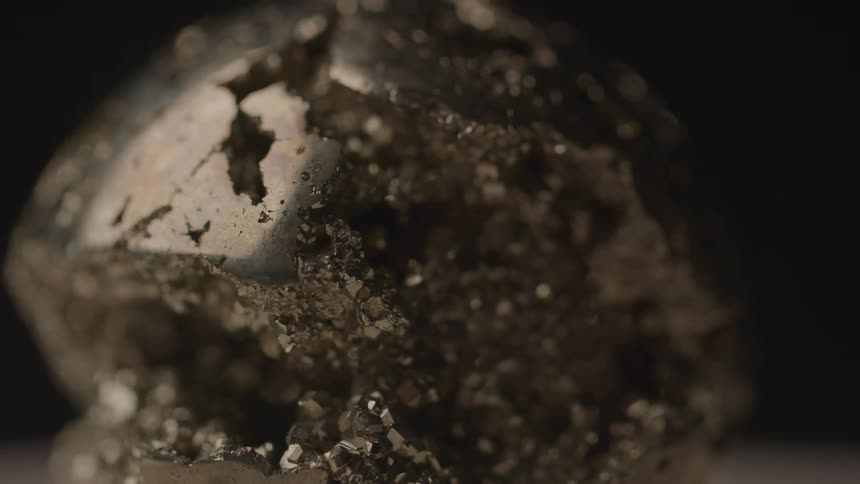 A close up of the rough and uneven texture of a metallic mineral shining against a dark background